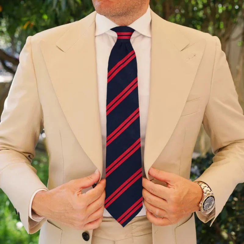 Man wearing a beige suit with a red and blue striped tie, outdoors.