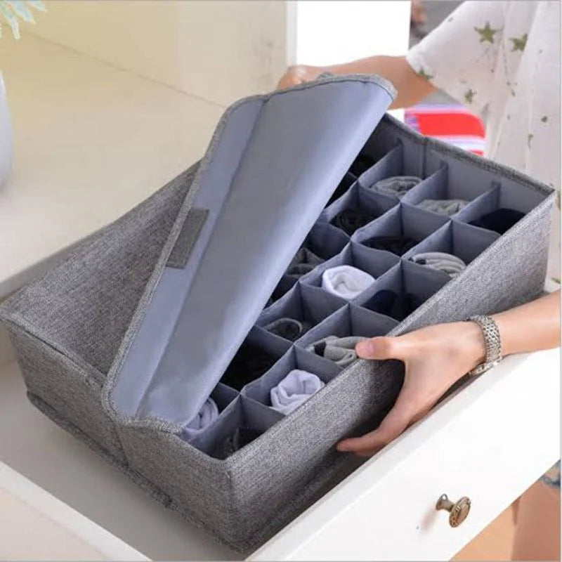 Gray fabric storage box with divided sections containing folded clothes on a white surface.