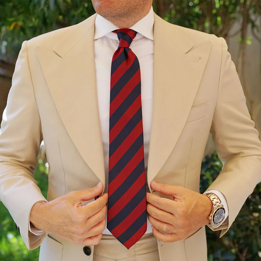Man wearing a beige suit with a red and navy striped tie, outdoors.